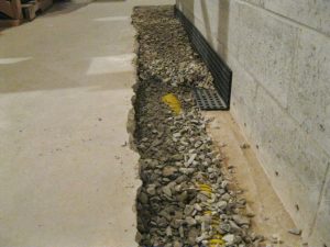 Interior French drain system installed along basement wall with gravel trench for water drainage and moisture control