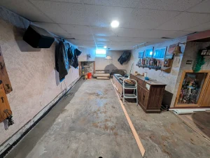 Interior French drain system installed along basement wall in Erie PA with concrete floor restored and sump pump drainage system in place.