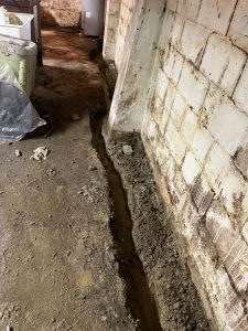 Interior French drain trench installation along a basement wall in Erie, PA to solve severe moisture and hydrostatic pressure problems.